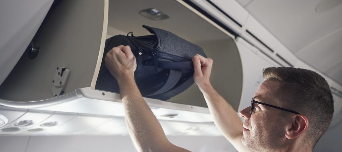 Man travel by airplane. Passenger putting hand baggage in lockers above seats of plane.