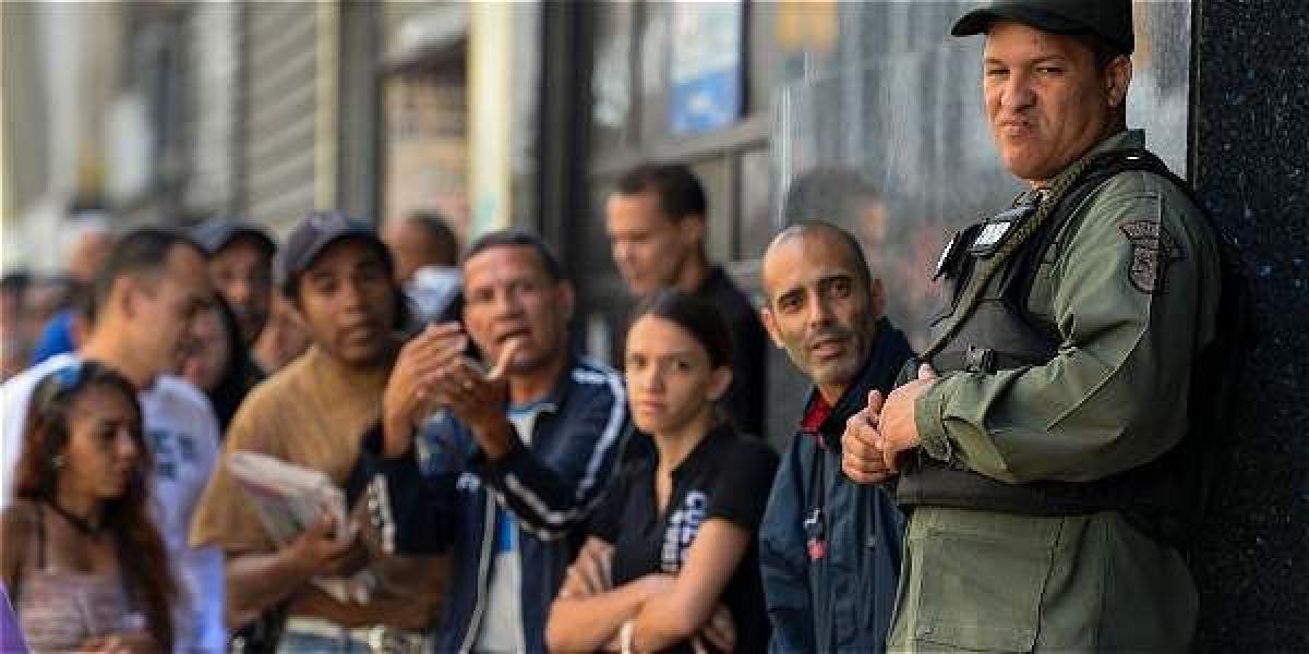 Un policía vigila a la gente que hace fila a las afueras de un banco en Caracas.