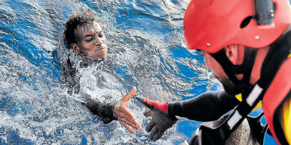 Un migrante es rescatado de las aguas del Mediterráneo por un miembro de la ONG Proactiva Brazos Abiertos, unas 20 millas náuticas al norte de Libia.