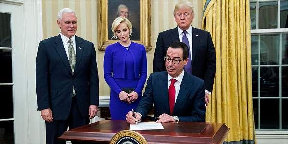El presidente de Donald Trump observa al nuevo secretario del Tesoro, Steven Mnuchin, firmar un documento acompañado por el vice presidente Mike Pence y la prometida de Mnuchin, Louise Linton.