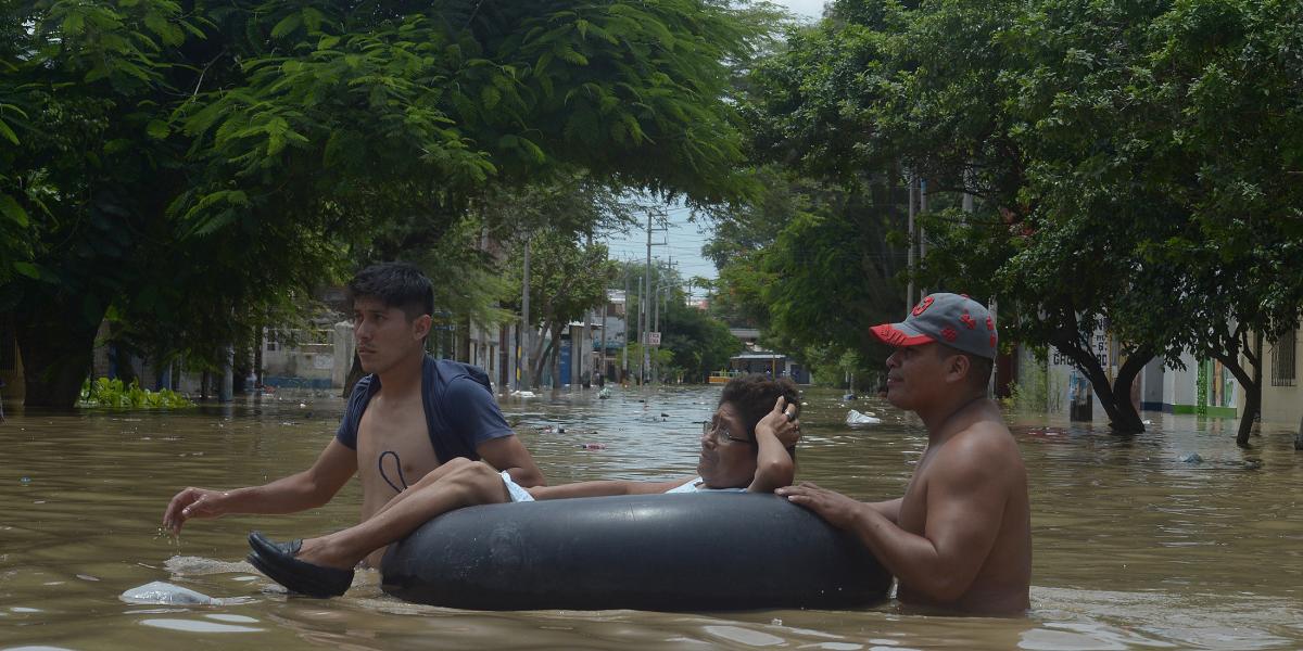 Residentes ayudan a una mujer a cruzar una calle inundada después de que los ríos se desbordaron a causa de las lluvias en Piura.