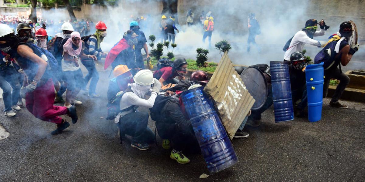 Activistas de la oposición venezolana se protegen tras una barricada improvisada durante los enfrentamientos con la policía en Caracas.