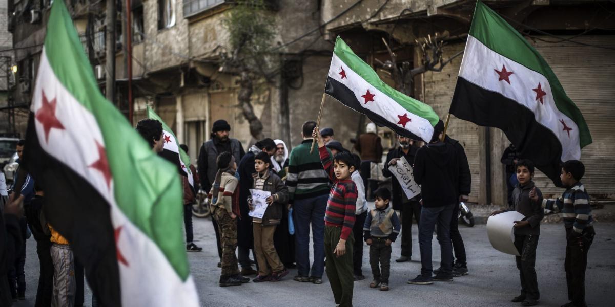 Un grupo de sirio ondea la bandera nacional 
siria durante una protesta en contra de los bombardeos de la aviación rusa en Duma.