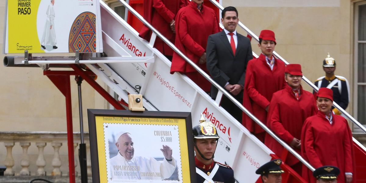 En primer plano, la estampilla oficial de la visita y, al fondo, la tripulación de Avianca que atenderá al Papa.