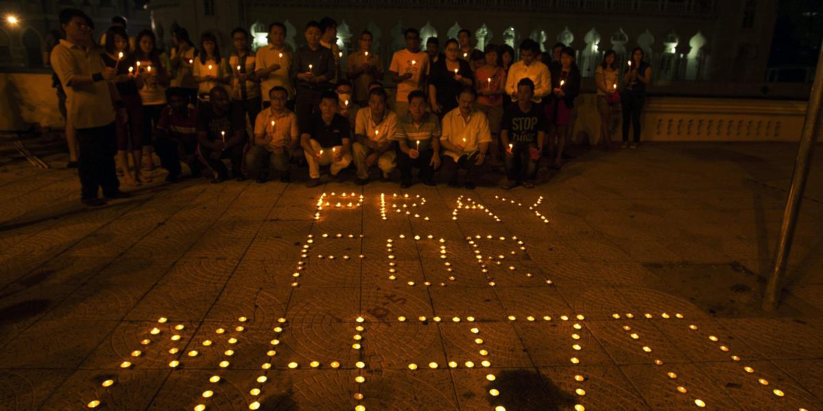 Varias personas posan frente a un conjunto de velas que conforman la frase "Rezar por MH370", durante una vigilia en memoria de las 239 personas que viajaban a bordo del avión de Malaysia Airlines.