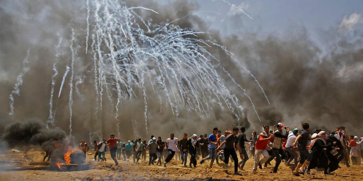 Varios palestinos corren para protegerse de los gases lacrimógenos que arrojan las fuerzas de seguridad israelíes en la frontera de la Franja de Gaza e Israel.