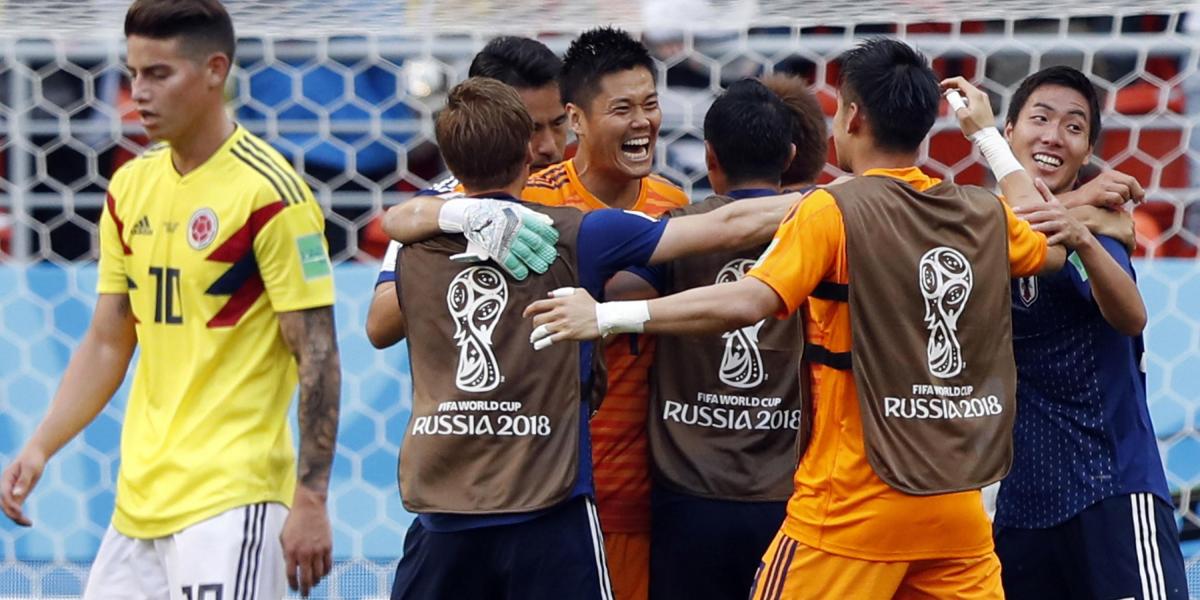 James Rodríguez se despide de la cancha con rostro de decepción, tras la victoria 2-1 de Japón, cuyos jugadores celebran el buen resultado.