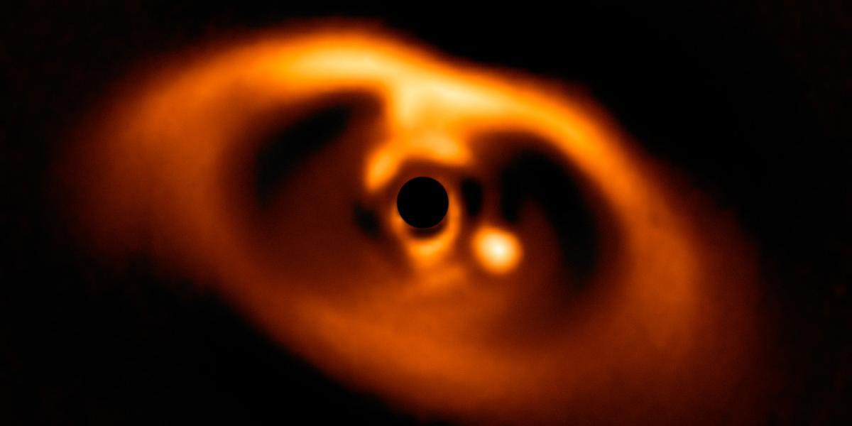 PDS 70b, el primer planeta en ser captado al nacer, puede apreciarse en la fotografía a la derecha del punto negro que hay en el centro de la nube de polvo y gas.
