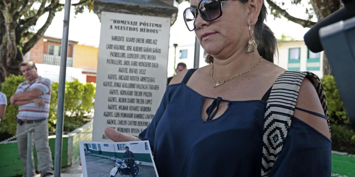 Alba Alicia Ocampo, esposa de policía que murió durante la toma, muestra la foto del uniformado frente a monumento en honor a los caídos.