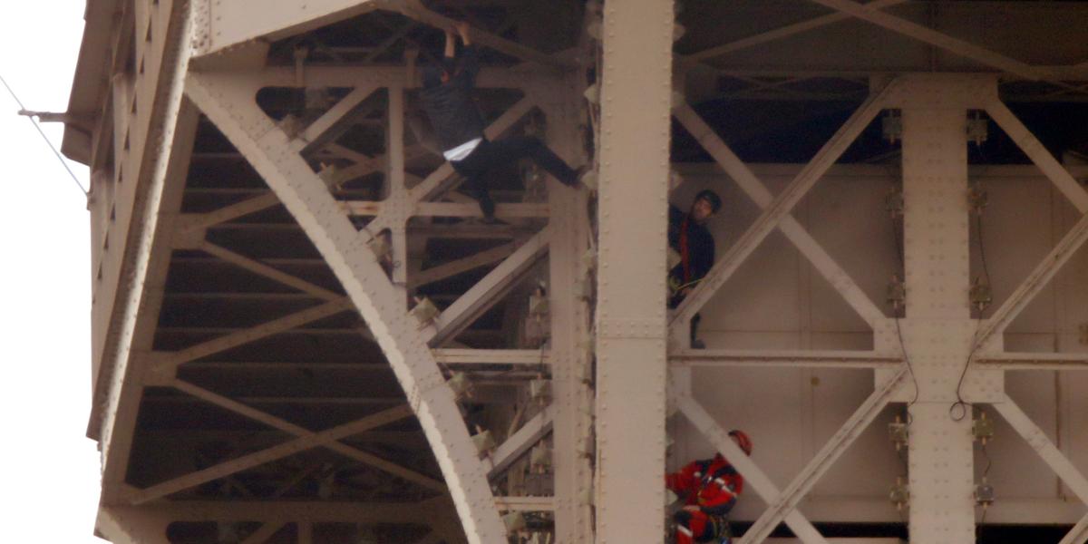 Los bomberos de Paris se acercan al hombre no identificado que intentó escalar la Torre Eiffel y provocó una salida de emergencia de las personas que estaban de visita.