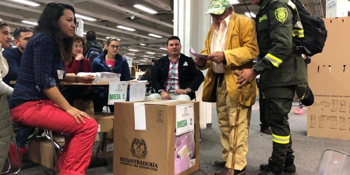En Corferias, en Bogotá, un policía ayuda a un hombre de la tercera edad a ejercer su derecho al voto.