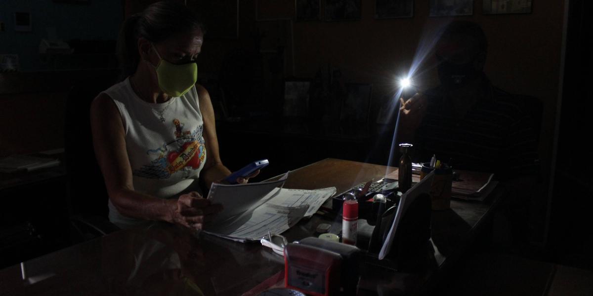 Una mujer revisa facturas mientras le ayudan a iluminarlas con un celular en un local comercial de San Cristóbal. El apagón no solo fue en Caracas. Se reportaron fallas electrias en otros cuatro estados.