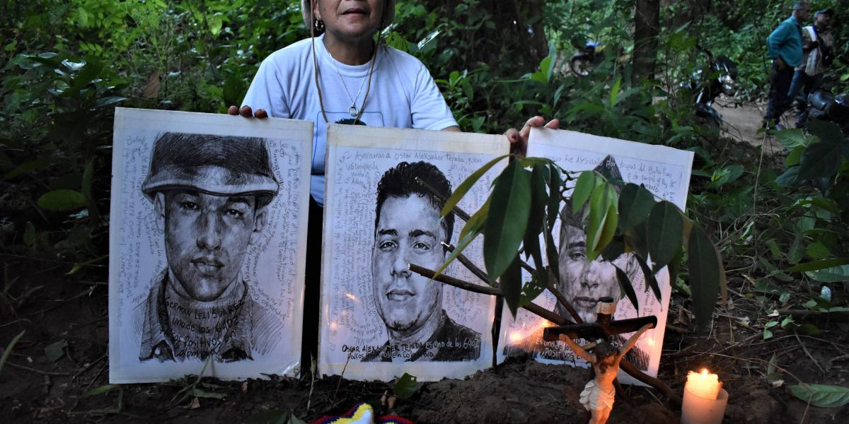Doris Tejada, madre de Óscar Morales, sostiene los retratos de su hijo (centro), Octavio Bilbao (der.) y Germán Leal (izq.) en el lugar donde fueron asesinados.