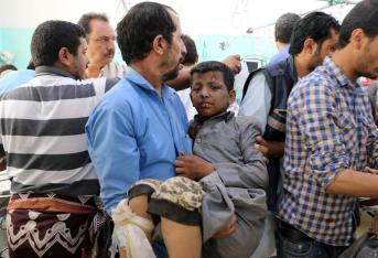 Un hombre lleva en brazos a un niño herido en el ataque a un bus en Saná, capital de Yemen.