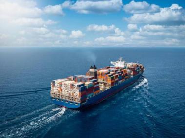 A large container cargo ship travels over calm, blue ocea