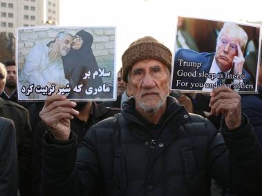 Un iraní sostiene un cartel en una ceremonia para rendir homenaje al general iraní Qasem Soleimani (i.) en Mashhad (Irán) el 5 de enero de 2020. En la otra una foto del presidente estadounidense Donald Trump.
