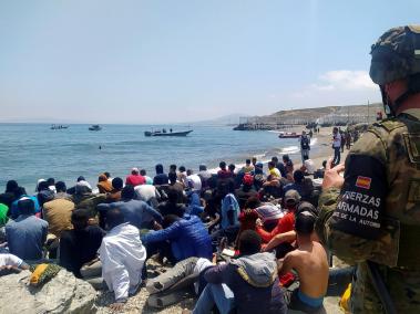 Un soldado del Ejército de Tierra observa a un grupo de inmigrantes que han logrado cruzar uno de los espigones fronterizos de Ceuta este martes en una avalancha de inmigrantes sin precedentes en España al registrarse la entrada en 24 horas de 5.000 personas (un tercio de ellas menores).