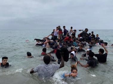 Un grupo de personas se hacen con una embarcación de las autoridades marroquíes en la playa de la localidad de Fnideq (Castillejos) para cruzar los espigones de Ceuta este martes en una avalancha de inmigrantes sin precedentes en España al registrarse la entrada en 24 horas de 5.000 personas (un tercio de ellas menores).