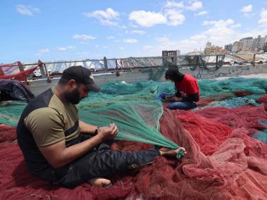 Los pescadores palestinos reparan sus redes antes de hacerse a la mar en el puerto principal de la ciudad de Gaza, después de que se levantara la prohibición de pescar tras un alto el fuego entre Israel y militantes palestinos en el enclave bloqueado por Israel.