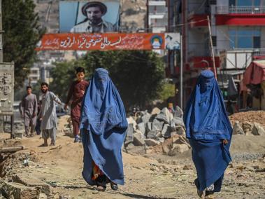 Una pancarta con una imagen del difunto comandante afgano Ahmad Shah Massoud instalada junto a edificios residenciales mientras mujeres afganas vestidas con burka caminan por una carretera en construcción en Kabul el 8 de septiembre de 2021.