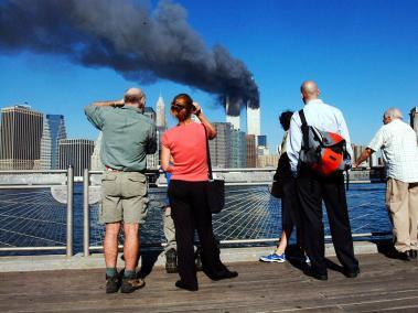 En esta foto de archivo, peatones al frente del río del Este, en Nueva York, miran cómo arden en llamas las Torres Gemelas.
