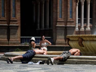 Dos jóvenes sumergen la cabeza en el agua de una fuente para refrescarse, en la Plaza de España de Sevilla.