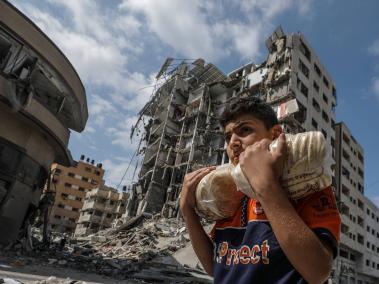 Un joven palestino cargado de pan pasa junto a edificios destruidos en Gaza.