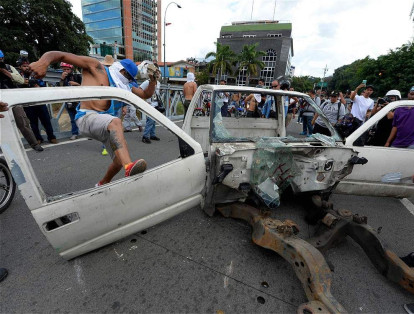 Los manifestantes desmantelan una vieja carcasa de un coche para hacer una barricada durante la marcha de opositores en Caracas.
