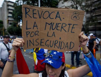 Una mujer sostiene un cartel junto a un grupo de personas que participan en la 'Toma de Caracas'.