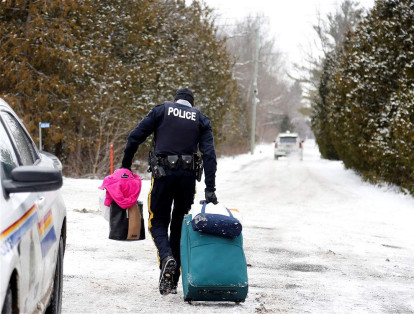 Un policía canadiense carga el equipaje de una de las familias que intentó ingresar al país por la frontera con Estados Unidos.