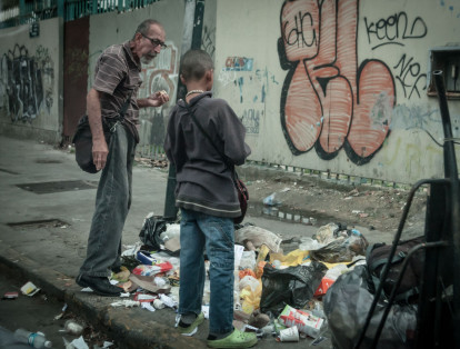 En la foto, un anciano y un niño comen alimentos que sacaron de la basura.