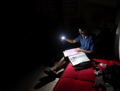 Por la falta de electricidad, Hugo Regalado lee el periódico con la ayuda de una linterna en medio de una oscura noche en la isla.