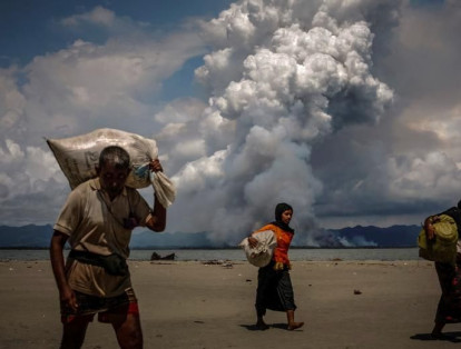 Se ve humo en la frontera con Myanmar cuando los refugiados rohinyás caminan por la orilla después de cruzar la frontera entre Bangladesh y Myanmar en barco.