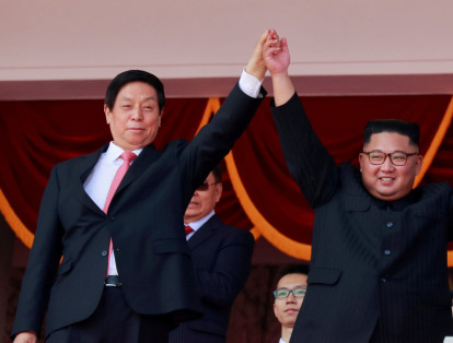 El dirigente norcoreano Kim Jong Un (derecha) prefirió mostrar su amistad con China, levantando la mano del enviado del presidente Xi Jinping (izquierda) cuando ambos saludaron a la multitud durante el desfile.