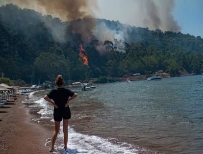 Una mujer observa desde una playa el bosque en llamas el 3 de agosto de 2021 en Mugla, mientras Turquía lucha contra los incendios forestales más letales en décadas.