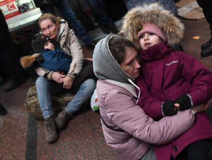 Dos mujeres se sientan en el suelo, mientras sostienen en sus brazos a sus hijos en la estación de tren de Lviv.