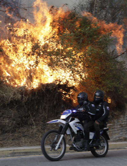 AME2193. QUITO (ECUADOR), 24/09/2024.- Agentes de la Policía de Ecuador pasan frente a un incendio forestal este martes, en el sector de Guapulo en Quito (Ecuador). EFE/ Santiago Fernández