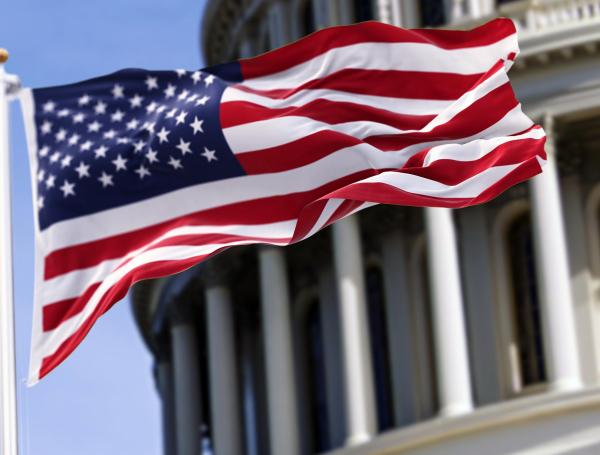 The flag of the united states of america flying in front of the capitol building blurred in the background. United states federal congress on Capitol hill in Washington D.C. Democracy and freedom.
