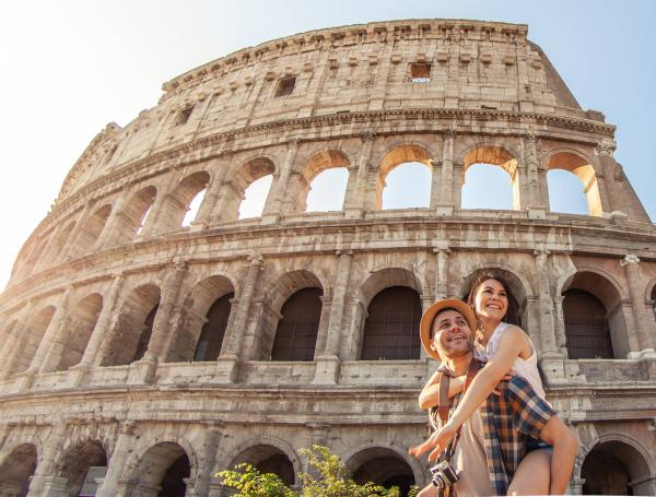 Una pareja conformada por un hombre y mujer abrazados al frente del Coliseo de Roma
