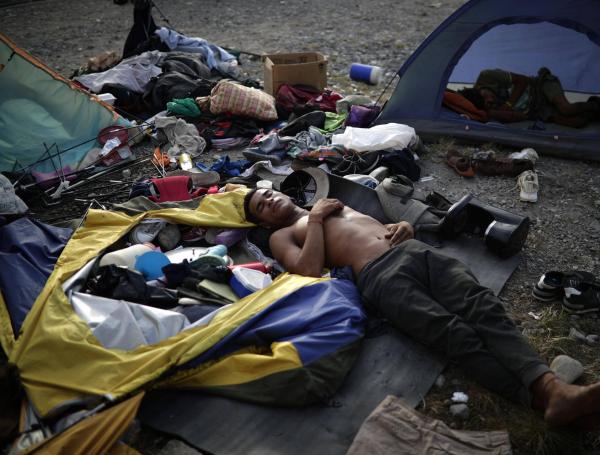 Un migrante duerme mientras decenas esperan su traslado.