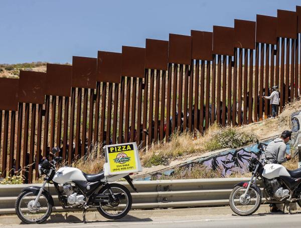 Repartidores de comida rápida entregan pedidos a migrantes en el muro fronterizo hoy, en la ciudad de Tijuana, Baja California.