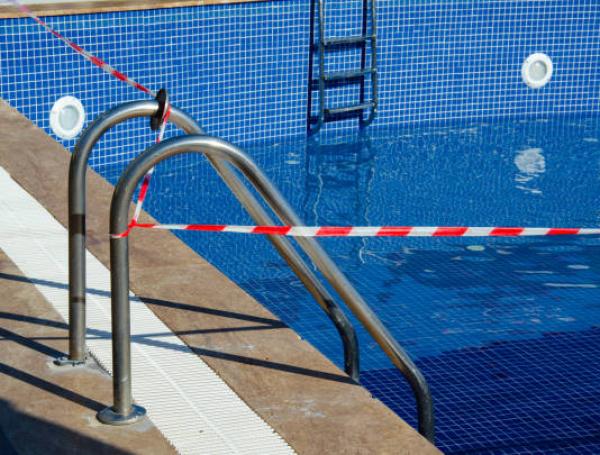 Red and white tape prohibits entry to swimming pool. Selective focus on pool with no-entry tape. Ban on visiting public places during the coronavirus epidemic