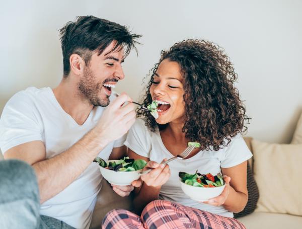 Happy man feeding his girlfriend with salad