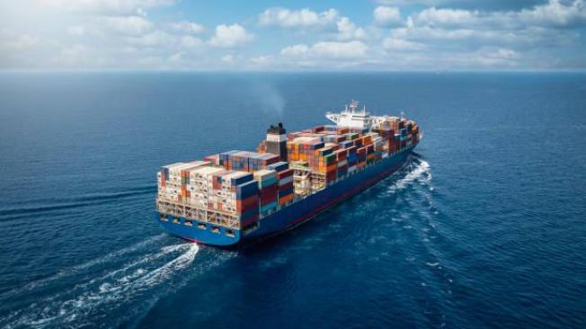 A large container cargo ship travels over calm, blue ocea