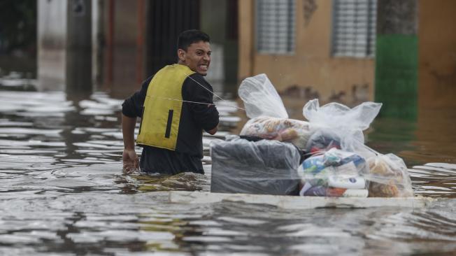 Un hombre camina con una tabla transportando suministros entre las calles inundadas este domingo, en el barrio Humaita, en Porto Alegre (Brasil).
