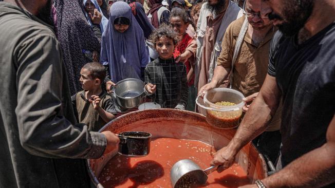 Personas se reparten porciones de comida de una gran olla en una cocina pública de Deir el-Balah, en el centro de la Franja de Gaza.