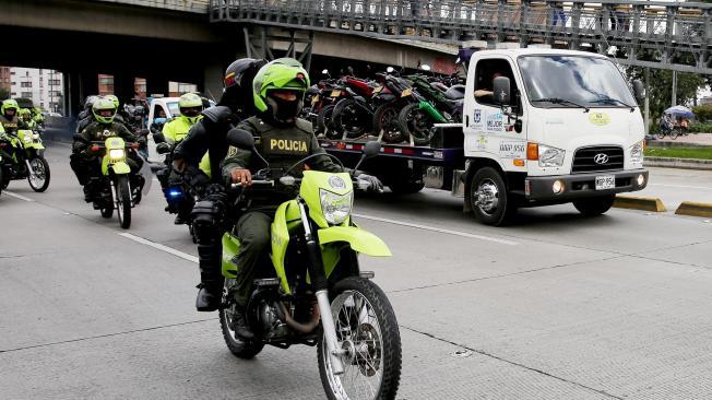 Una grúa con motocicletas inmovilizadas es escoltada por miembros de la policía.