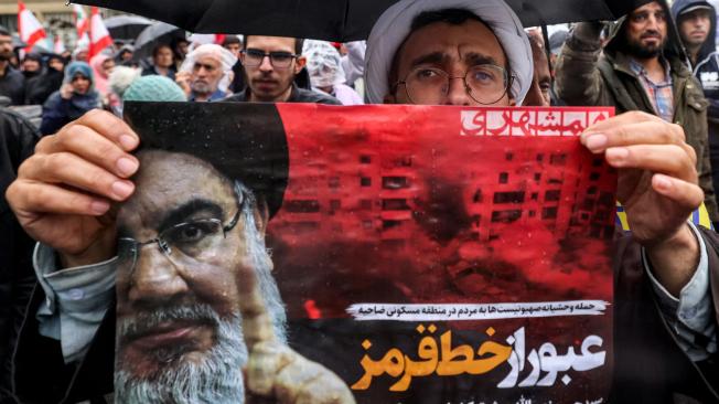 Un clérigo musulmán chií sostiene un cartel en el que se lee «cruzar una línea roja» en persa junto a una imagen de Hassan Nasrallah.