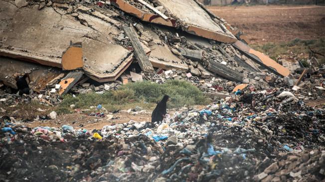 Una mujer busca objetos rescatables entre un montón de basura junto a los escombros de un edificio derrumbado en el campo de refugiados palestinos de Bureij, en el centro de la Franja de Gaza.