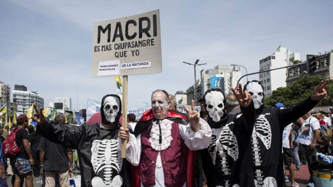 Manifestantes vestidos con trajes de vampiro y esqueleto sostienen una señal contra el presidente Mauricio Macri.
